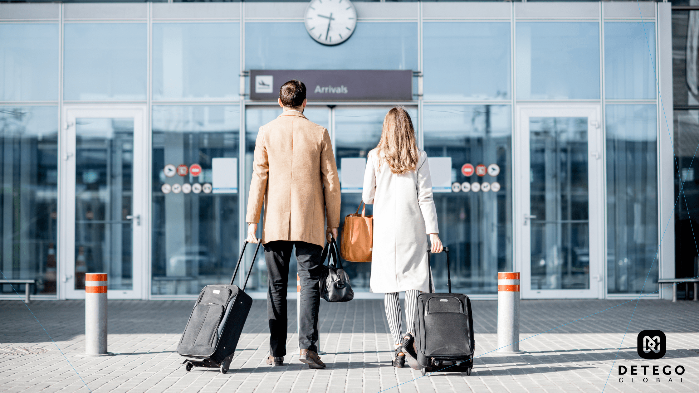 A man and a woman stand, luggage in hand, facing the glass entryway of an airport