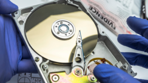 Blue gloved hands holding a hard disk platter marked as "evidence"