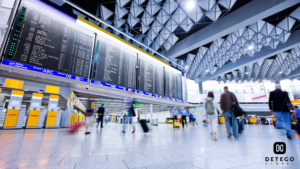 People walk past airline arrival and departure boards in an airport hall