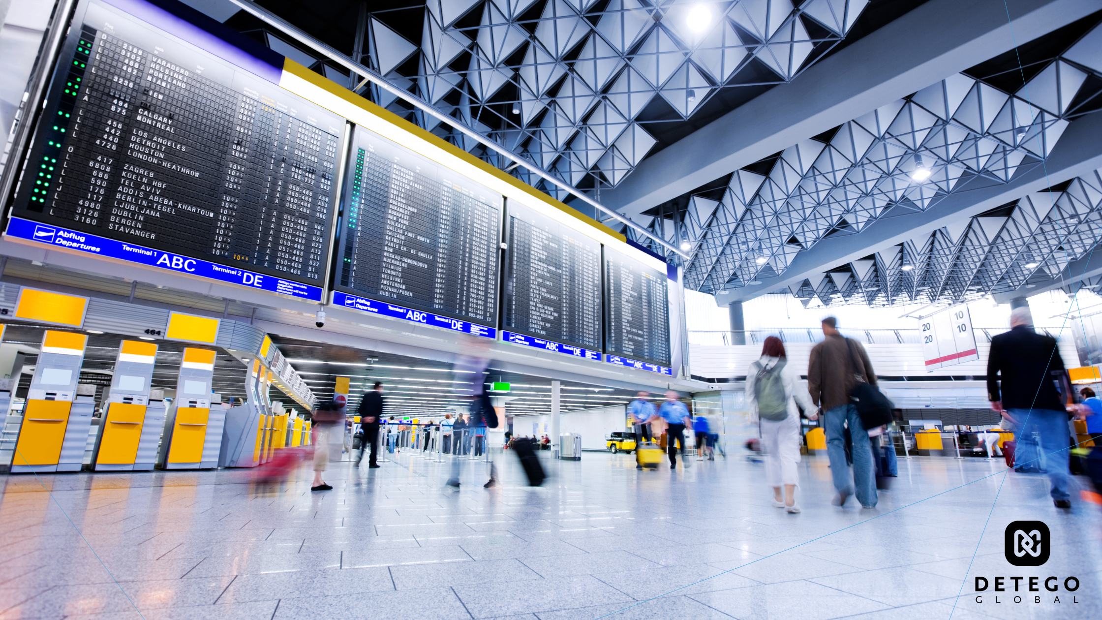 People walk past airline arrival and departure boards in an airport hall