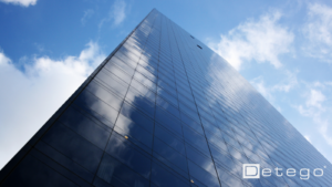 A view of a glass skyscraper, looking up from the ground towards the blue sky